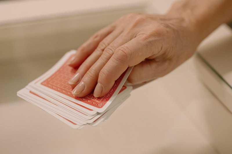 A person's hand selecting cards from a fan spread across a glass table, capturing the moment of strategic choice in card play