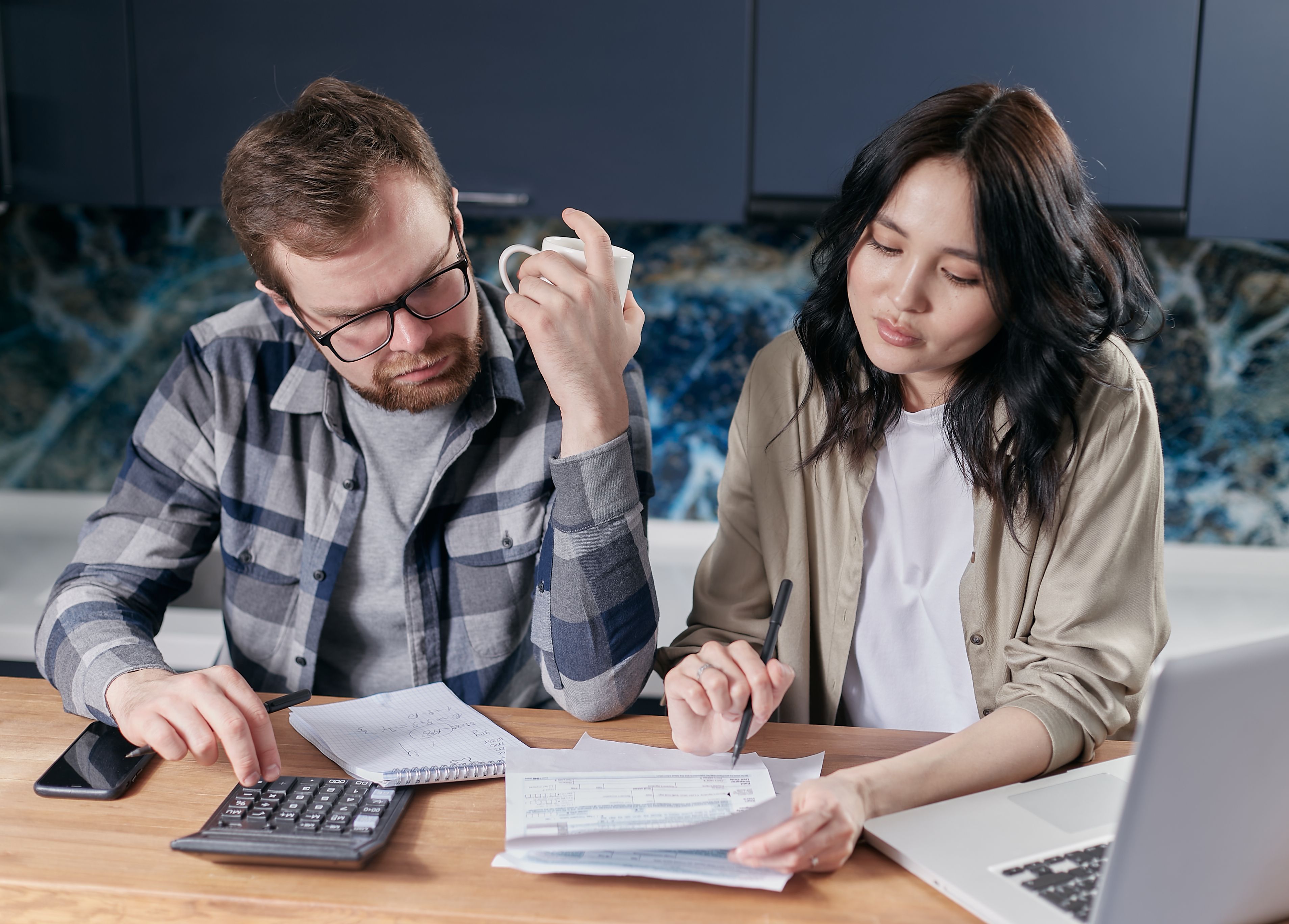 Young couple reviewing household bills and budget using a calculator and laptop at their kitchen table